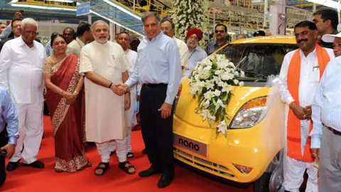 AFP Narendra Modi, then governor of Gujarat, shakes hands with the chair of Tata group at a new factory. A yellow car is adorned with white flowers.