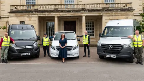 Dominic Argar A woman standing in front of three vehicles with men in high-vis