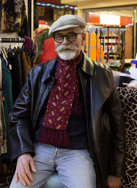 Rebecca Russell A man with a beard and glasses in front of a clothing stall