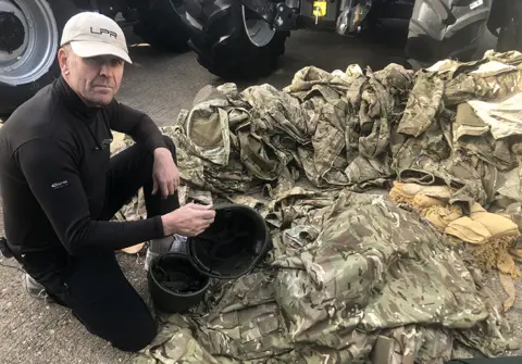 Wozza sits next to pile of military uniforms