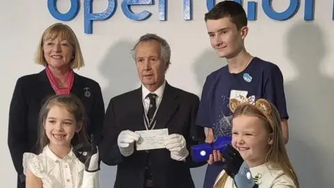 families Joshua and Thalia with arms in a cheque presentation