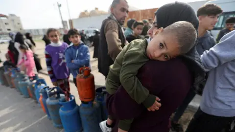 Reuters A woman carries a child as Palestinians gather to fill liquid gas cylinders, during a temporary truce between Hamas and Israel, in Rafah in the southern Gaza Strip