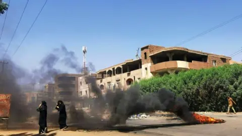 AFP Sudanese women walk in front of tyres set ablaze by anti-coup demonstrators in the capital Khartoum, following calls for civil disobedience to protest last month's military coup, on November 7, 2021.