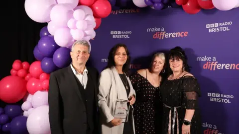 BBC Barton Hill Rugby Football Club Charity Café volunteers, pictured by pink and purple balloons and a purple backdrop printed with the BBC Radio Bristol and Made A Difference logos