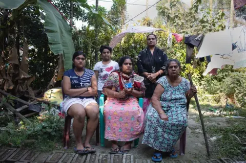 Swastik Pal Mallika Kar (seated, middle) with her family in Bishnupur, West Bengal. Kar is a widow. On her left is her daughter Manisha Kar and on her right is her mother Premlata Dhara. Standing behind is her sister in law Barnali Dhara and her son, Noel Dhara - West Bengal welfare case study