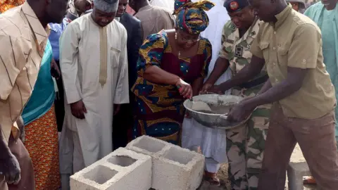 Getty Images Ngozi Okonjo-Iweala using a trowel to scoop mortar from a pan