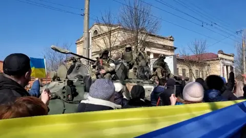 BBC Pro-Ukrainian protesters pass Russian soldiers on a tank during a rally in Kherson in March, 2022