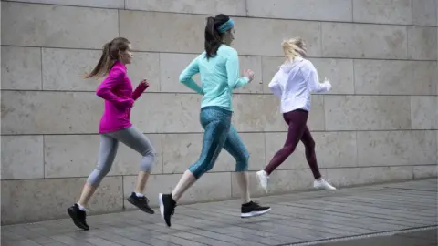 Getty Images Rear view of three woman jogging on footpath along side a wall. - stock photo