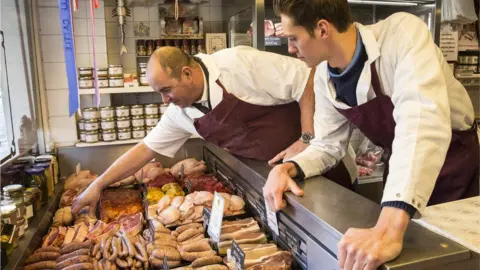 Mint Images Butchers stand at a counter with raw sausages and other meats