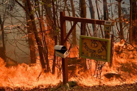 Getty Images A mailbox and signpost burn amid heavy flames