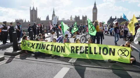 PA Media Extinction Rebellion climate protestors with flags and banners sitting on Westminster Bridge