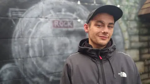 BBC Mickey standing outside by a wall