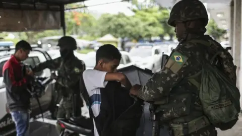 EPA A soldier controls passers-by in Rio de Janeiro, Brazil, 23 February 2018.