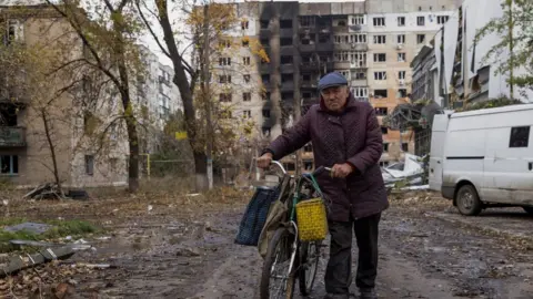 Reuters A man walks with his bicycle in front of bombed-out residential buildings in Avdiivka, eastern Ukraine. Photo: October 2023