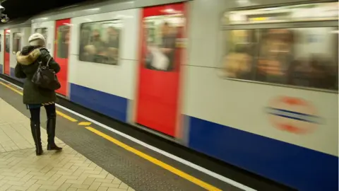 Getty Images/Gregory Adams Woman waiting as a train arrives in the station