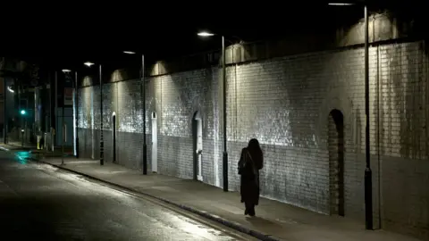 Getty Images A woman walks alone along a street at night