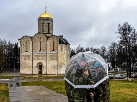 Vasily Maximov / AFP Cadets shelter from the rain under an umbrella in front of a church in the town of Vladimir, Russia