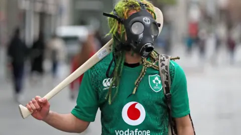 Niall Carson A man wearing a gas mask and carrying a hurling stick in Dublin on St Patrick's day