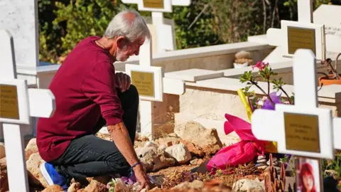 PA Media A man lays flowers on a grave