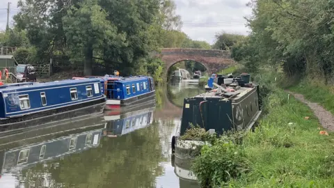 Three canal boats moored on the Kennet and Avon canal in the Pewsey Vale with a bridge in the distance