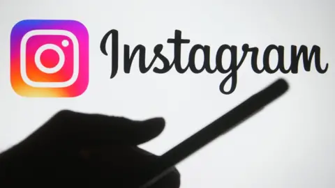 Getty Images The silhouette of a hand holding a smartphone is seen in front of the Instagram logo