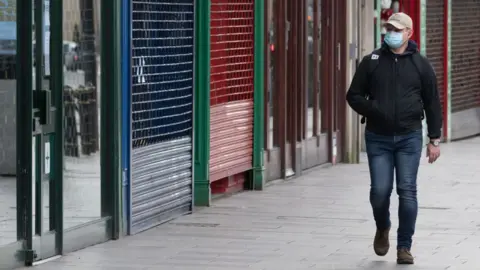 Getty Images Man wearing face mask walking past shuttered shops in Cardiff