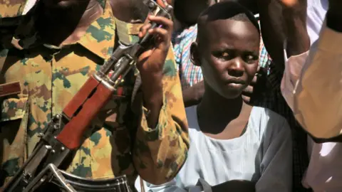 Getty Images A child looks on as Sudan's prime minister visits a camp for internally displaced people (IDP) in El-Fasher, the capital of the North Darfur state, on November 04, 2019. - Sudan's prime minister Abdalla Hamdok's one-day visit was his first as prime minister to the devastated region, where a conflict that erupted in 2003 has left hundreds of thousands dead and millions displaced. He said his government was working toward bringing peace to war-torn Darfur as he met hundreds of victims of the conflict who demanded swift justice.