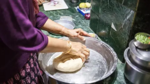 Getty Images A woman prepares dough for traditional Indian bread chapati in the kitchen at Boisahabi Tea Estate, Assam, India on 7 March, 2019.