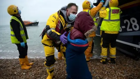 Getty Images A migrant is helped ashore by someone from the RNLI