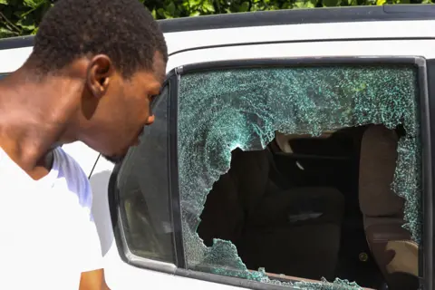 Valerie Baeriswyl / AFP A man looks at bullet holes in a car outside of the presidential residence in Port-au-Prince, Haiti, on 7 July 2021