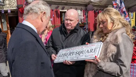 PA Media The Prince of Wales is presented with an Albert Square street sign from Steve McFadden and Letitia Dean