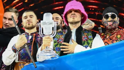 AFP Members of the band Kalush Orchestra pose on stage with the winner's trophy and Ukraine's flags after their Eurovision win