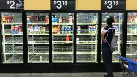 Reuters Woman looks over bare refrigerator shelves in a Walmart in Houston