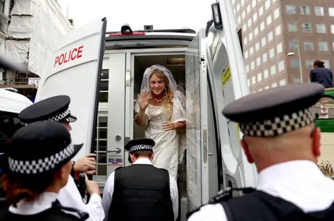 Tom Nicholson / Reuters An activist wearing a wedding dress stands in a police vehicle during an Extinction Rebellion protest in London on 31 August 2021