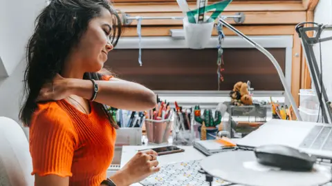 Getty Images A woman rubs her shoulder whilst working at home