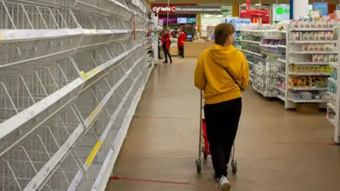 Getty Images A woman walks by empty shelves in a supermarket in Moscow. There has been shortages of women's sanitary pads, diapers, and sugar