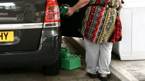 Getty Images A woman fills her car with fuel alongside two jerry cans at forecourt in London