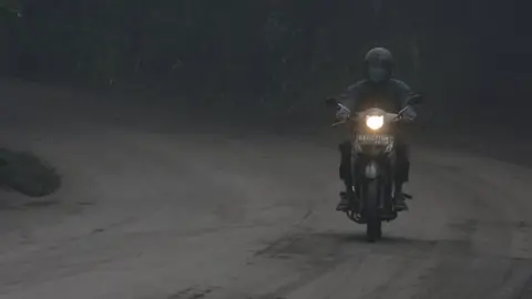 Reuters/Antara A motorist rides his motorbike during a shower of ash and rain from Mount Agung