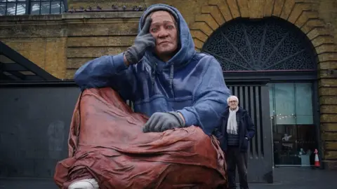 PA Media The sculpture next to Jonathan Pryce