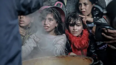 Getty Images Palestinian children wait in front of a big pot of food distributed by charity organizations in Gaza City, Gaza on February 26, 2024