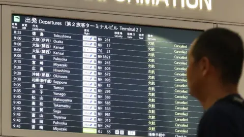 AFP A man looks at the flight information board at the Haneda International airport in Tokyo on 12 October, 2019.