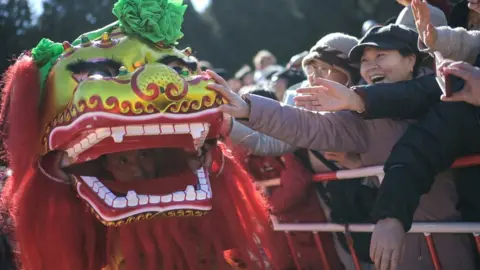 2024 年 2 月 15 日，北京，龙年初六，庙会上的舞狮表演中，人们试图触摸狮子面具。