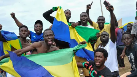 Rex/Shutterstock Gabonese people wave flags as they celebrate the military's takeover.