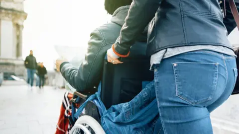 Getty Images A stock photo of a man being pushed in a wheelchair