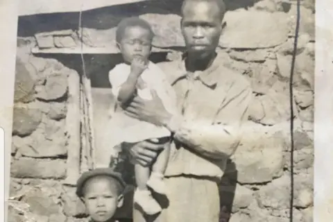 Agnes Sithole A photo of Agnes Sithole with her younger sister and father outside the house she was born in