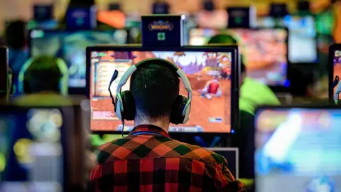 Getty Images The back of a man's head who's wearing headphones and playing World of Warcraft on a computer screen