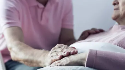 Getty Images Older couple - with one placing hand on woman's who is lying down