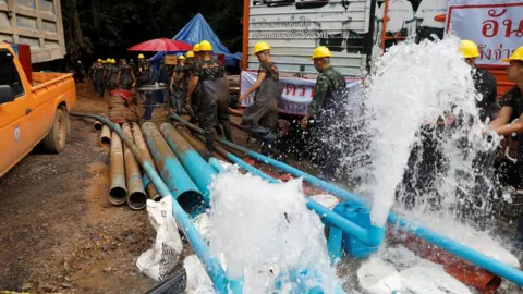 Reuters Soldiers and rescue workers walk past water pumped out of Tham Luang cave complex