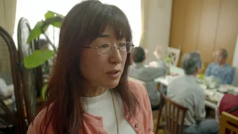 Akiko Saito with people eating lunch behind her