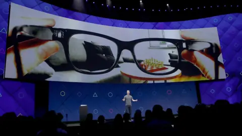 Getty Images Mark Zuckerberg on stage with a large screen above him showing a pair of glasses.